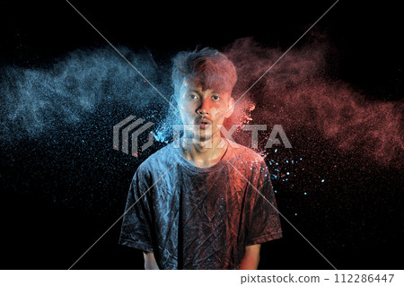 Asian man splashed with colorful holi powder and having fun isolated on black background. Asian man splashed with colorful holi powder and having fun isolated on black background. 112286447