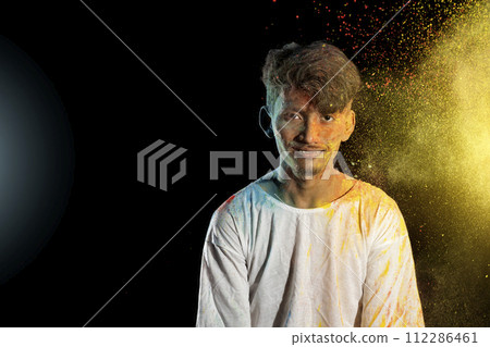Asian man splashed with colorful holi powder and having fun isolated on black background. Asian man splashed with colorful holi powder and having fun isolated on black background. 112286461