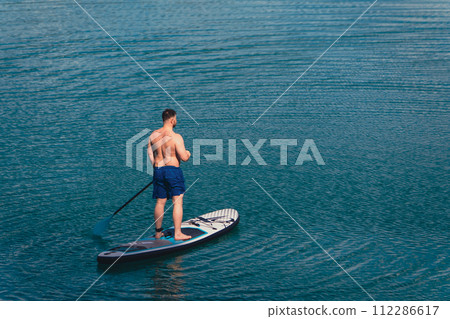 man balancing on supboard paddling 112286617