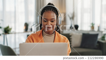 Laptop, headphones and young woman in living room listening to music, playlist or album in modern apartment. Technology, smile and young African person streaming song on computer in lounge at home. 112286990