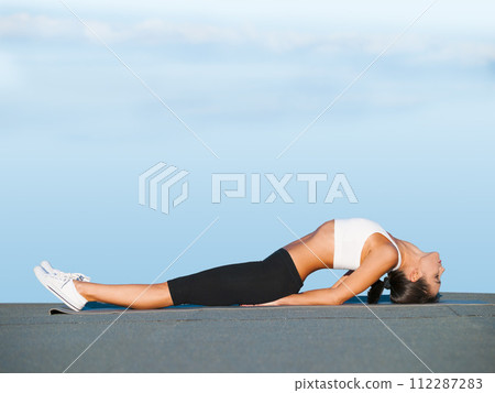 Stretching, back and woman outdoor with yoga, exercise and holistic workout on ground. Summer, pilates and person on floor for mobility and flexibility of spine muscle with routine on blue sky 112287283