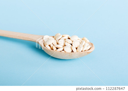 Heap of white pills on colored background. Tablets scattered on a table. Pile of red soft gelatin capsule. Vitamins and dietary supplements concept 112287647