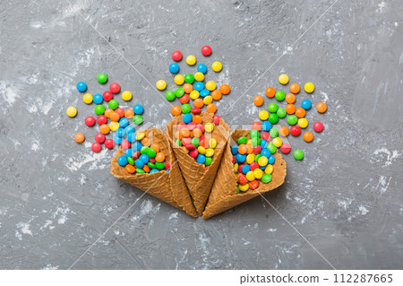 waffle cone full of assorted traditional candies falling out on colored background with copy space. Happy Holidays sale concept 112287665