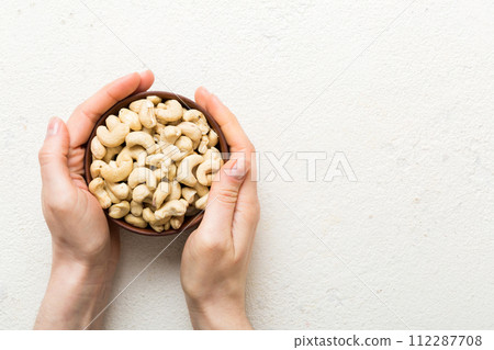 Woman hands holding a wooden bowl with cashew nuts. Healthy food and snack. Vegetarian snacks of different nuts 112287708