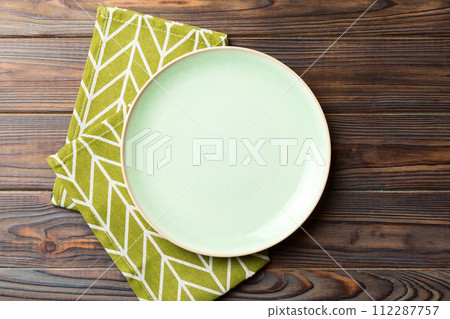 Top view on colored background empty round green plate on tablecloth for food. Empty dish on napkin with space for your design Top view on colored background empty round green plate on tablecloth for food. Empty dish on napkin with space for your design 112287757
