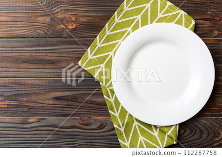 Top view on colored background empty round white plate on tablecloth for food. Empty dish on napkin with space for your design Top view on colored background empty round white plate on tablecloth for food. Empty dish on napkin with space for your design 112287758