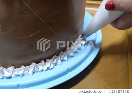 A woman pastry chef with a pastry bag in her hands squeezes cream on a cake in a home kitchen. Professional chef at work on bakery kitchen. culinary, baking and cooking food concept, home cooking 112287858