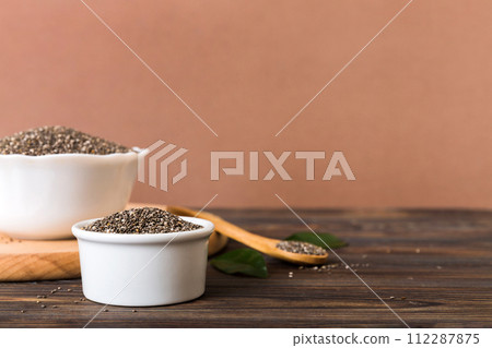 Chia seeds in bowl and spoon on colored background. Healthy Salvia hispanica in small bowl. Healthy superfood Chia seeds in bowl and spoon on colored background. Healthy Salvia hispanica in small bowl. Healthy superfood 112287875