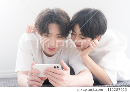Couple lying down in the living room while watching a movie on their smartphone, close-up Couple lying down in the living room while watching a movie on their smartphone, close-up 112287913