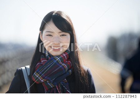 祝考生好運！一個可愛的高中女孩戴著圍巾，看著鏡頭，看著秋冬季入學考試的前視圖 112287943