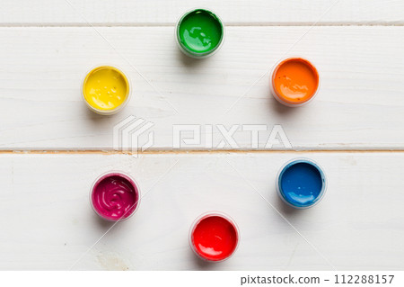 jars with gouache of different colors on Colored background. hobby painting. Top view with empty space. workplace for creativity. home teaching concept drawing 112288157