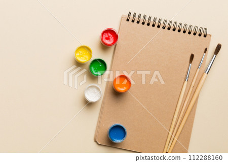 Album pages and paints, pencils, brush on a colored background. Top view with empty space. workplace for creativity. home teaching concept drawing 112288160