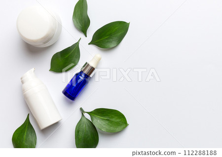 Organic cosmetic products with green leaves on white background. Copy space, flat lay Organic cosmetic products with green leaves on white background. Copy space, flat lay 112288188