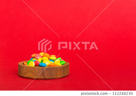 Multicolored candies in a bowl on a colored background. birthday and holiday concept. Top view with copy space Multicolored candies in a bowl on a colored background. birthday and holiday concept. Top view with copy space 112288230
