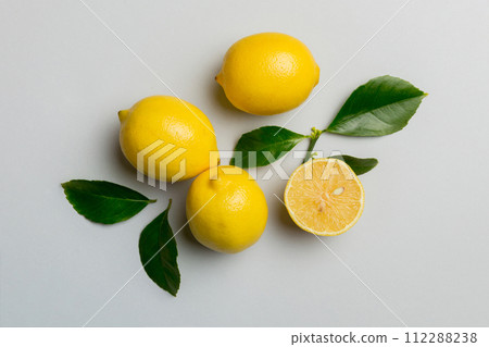 Many fresh ripe lemons with green leaves on colored background, top view, space for text 112288238