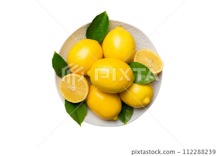 Fresh cutted lemon and whole lemons over round plate isolated on white background. Food and drink ingredients preparing. healthy eating theme top view with copy space 112288239