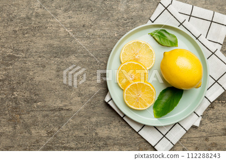 Fresh cutted lemon and whole lemons over round plate on colored background. Food and drink ingredients preparing. healthy eating theme top view vith copy space Fresh cutted lemon and whole lemons over round plate on colored background. Food and drink ingredients preparing. healthy eating theme top view vith copy space 112288243