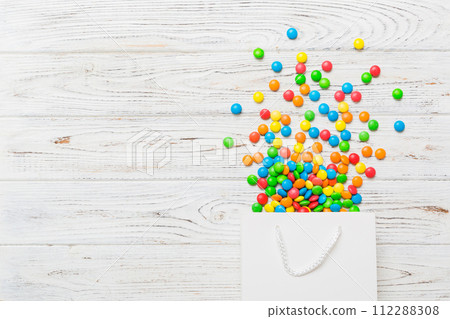 shopping paper gift bag in corner full of assorted traditional candies falling out on colored background with copy space. Happy Holidays sale concept shopping paper gift bag in corner full of assorted traditional candies falling out on colored background with copy space. Happy Holidays sale concept 112288308