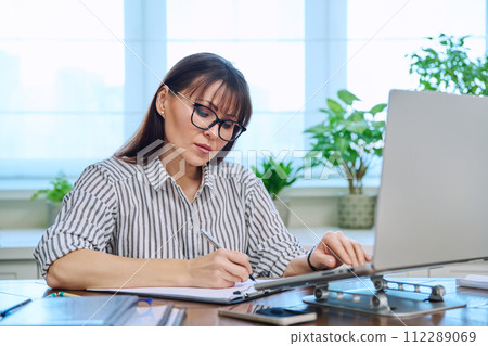 40s woman working with computer papers, remote workplace in home office 112289069
