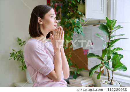 Profile view close-up of young woman's face with hands folded in prayer, dreams 112289088
