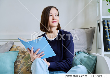Young woman reading book, relaxed sitting on couch at home 112289102