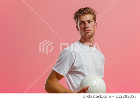 A man is holding a white soccer ball and standing in front of a pink background 112289355