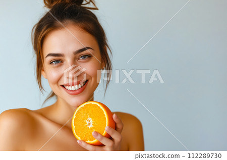 Woman with orange in her hand and orange slice on her face smiles for the camera. Generative AI 112289730