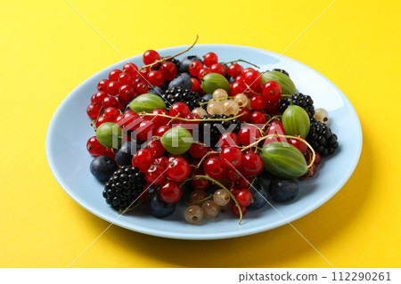 Ripe berries in a plate on a yellow background. Ripe berries in a plate on a yellow background. 112290261