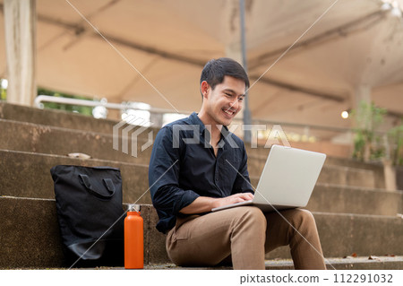 Asian businessman with reusable eco friendly ecological cup using laptop and sitting outside the office building. Eco friendly, sustainable lifestyle concept Asian businessman with reusable eco friendly ecological cup using laptop and sitting outside the office building. Eco friendly, sustainable lifestyle concept 112291032