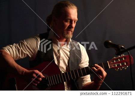 Portrait of classic mature musician playing acoustic guitar during stage performance and singing to microphone 112291671