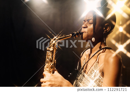 Side view portrait of young woman playing saxophone music on stage in golden lights copy space 112291721