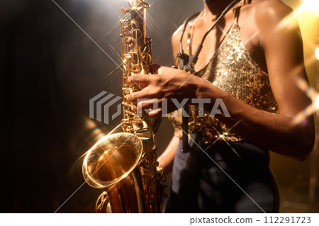 Close up of unrecognizable female musician playing jazz music focus on golden saxophone, copy space Close up of unrecognizable female musician playing jazz music focus on golden saxophone, copy space 112291723