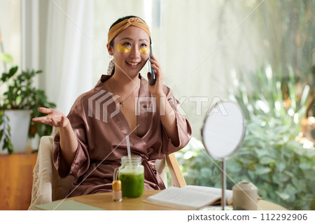 Portrait of smiling woman with undereye patches calling friend share news and gossips Portrait of smiling woman with undereye patches calling friend share news and gossips 112292906