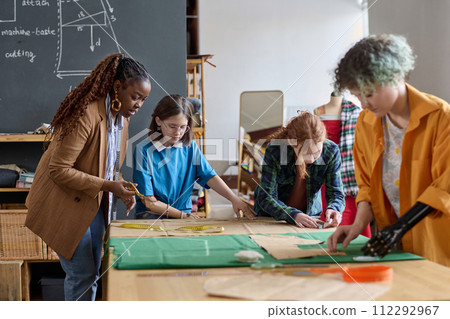 Diverse group of girls in tailoring class at atelier workshop with Black woman helping copy space 112292967