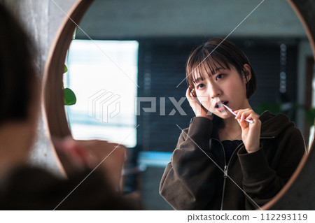 A woman brushing her teeth in front of the bathroom mirror in the morning 112293119