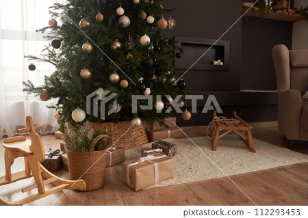 Christmas decor in domestic, cosy living room with christmas tree, wooden rocking chair, gifts, sledge, carpet. Background with copy space. Concept of Christmas, celebration, magic. Christmas decor in domestic, cosy living room with christmas tree, wooden rocking chair, gifts, sledge, carpet. Background with copy space. Concept of Christmas, celebration, magic. 112293453