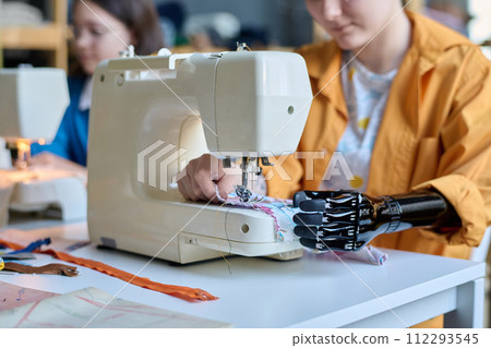 Close up of teenage girl with prosthetic hand using sewing machine in inclusive atelier studio copy space 112293545