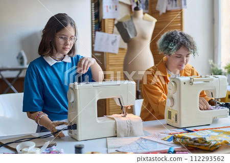 Portrait of two young girls with disability using sewing machines in school or vocational training class 112293562