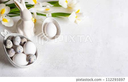 Easter white holiday card. Natural colors eggs in figured bowls, ceramic bunny, flowers. Copy space. Easter white holiday card. Natural colors eggs in figured bowls, ceramic bunny, flowers. Copy space. 112293897