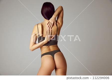 Rear view photo of young brunette woman brings her hands behind her back showing flexibility against grey studio background. Rear view photo of young brunette woman brings her hands behind her back showing flexibility against grey studio background. 112294006