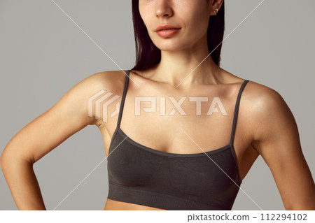 Cropped portrait of young female model demonstrate her smooth and tanned decollate zone against grey studio background. 112294102