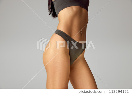 Cropped photo of young woman with slim body and smooth skin against grey studio background. Model with fit figure. Cropped photo of young woman with slim body and smooth skin against grey studio background. Model with fit figure. 112294131
