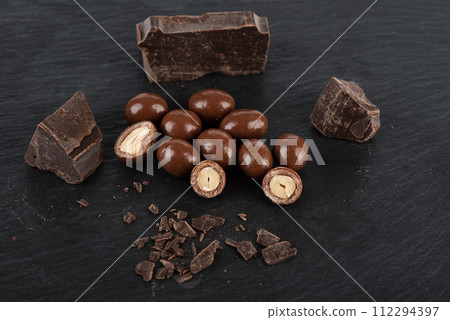 Dark chocolate glazed peanuts and chocolate chunks on a stone background. Dark chocolate glazed peanuts and chocolate chunks on a stone background. 112294397