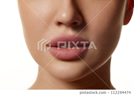 Cropped close-up image of beautiful female face, plump lips with nude lipsticks makeup isolated against white studio background. Lip augmentation 112294474