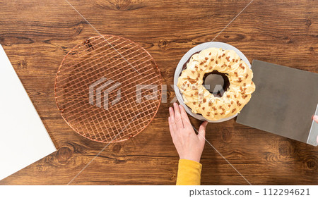 Flat lay. Carefully placing the gingerbread bundt cake, adorned with salted caramel frosting and gingerbread sprinkles, into a white paper bundt cake box with a clear window for gifting. 112294621