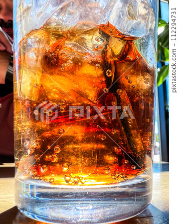 A close-up shot showcases a refreshing glass filled with ice cubes and soda pop, placed on a restaurant table, inviting the viewer to enjoy a cool and fizzy beverage. 112294731