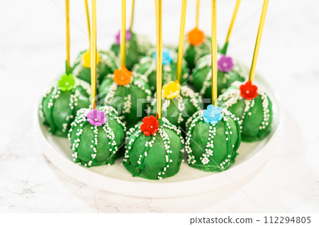 Cactus-shaped cake pops, beautifully decorated with luster dust, sugar flowers, and white sprinkles, arranged in celebration of Cinco de Mayo. Cactus-shaped cake pops, beautifully decorated with luster dust, sugar flowers, and white sprinkles, arranged in celebration of Cinco de Mayo. 112294805