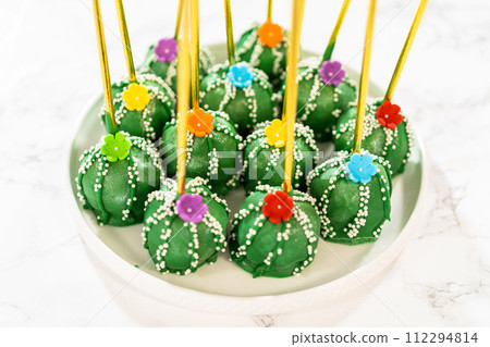 Cactus-shaped cake pops, beautifully decorated with luster dust, sugar flowers, and white sprinkles, arranged in celebration of Cinco de Mayo. Cactus-shaped cake pops, beautifully decorated with luster dust, sugar flowers, and white sprinkles, arranged in celebration of Cinco de Mayo. 112294814