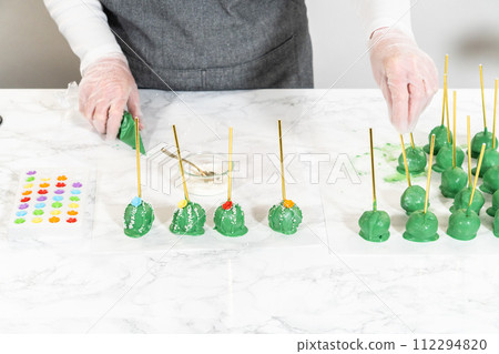 Decorating cactus cake pops with luster dust, sugar glower, and white sprinkles for the Cinco de Mayo celebration. 112294820