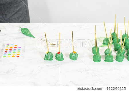 Decorating cactus cake pops with luster dust, sugar glower, and white sprinkles for the Cinco de Mayo celebration. Decorating cactus cake pops with luster dust, sugar glower, and white sprinkles for the Cinco de Mayo celebration. 112294825